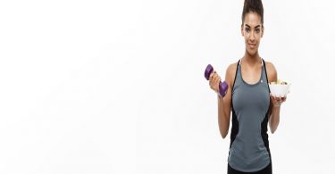 Healthy and Fitness concept - Beautiful sporty African American on diet holding dumbbell and fresh salad on hands. Isolated on white studio background.